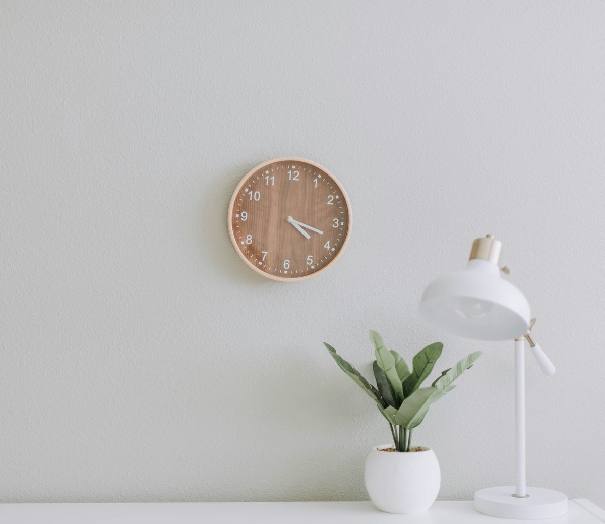 Bureau épuré avec horloge en bois, lampe blanche et plante verte